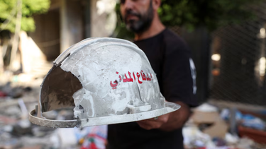 Un hombre sostiene un casco dañado en el que se lee Protección Civil tras el ataque de Israel a Beirut.
